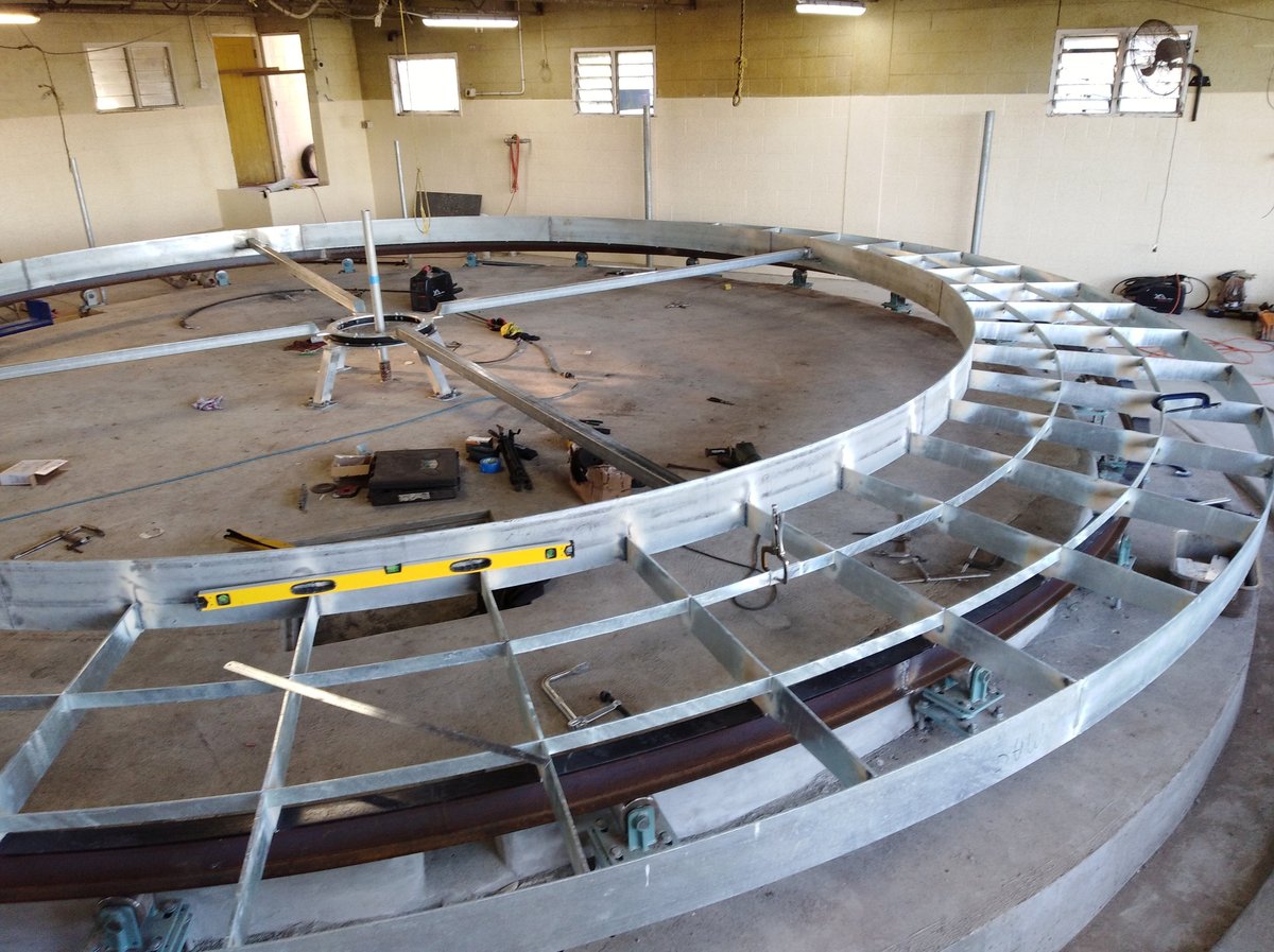 Large circular pool under construction with metal framing and white curved walls in an indoor warehouse facility